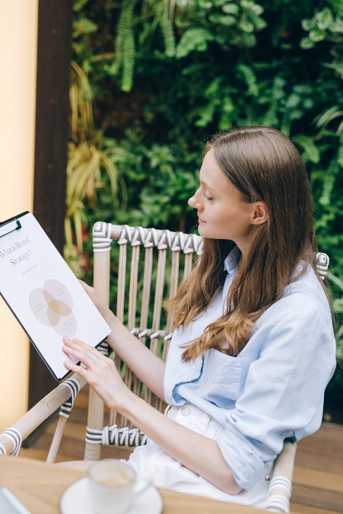 A woman reviews a business document while sitting outdoors with greenery in the background.